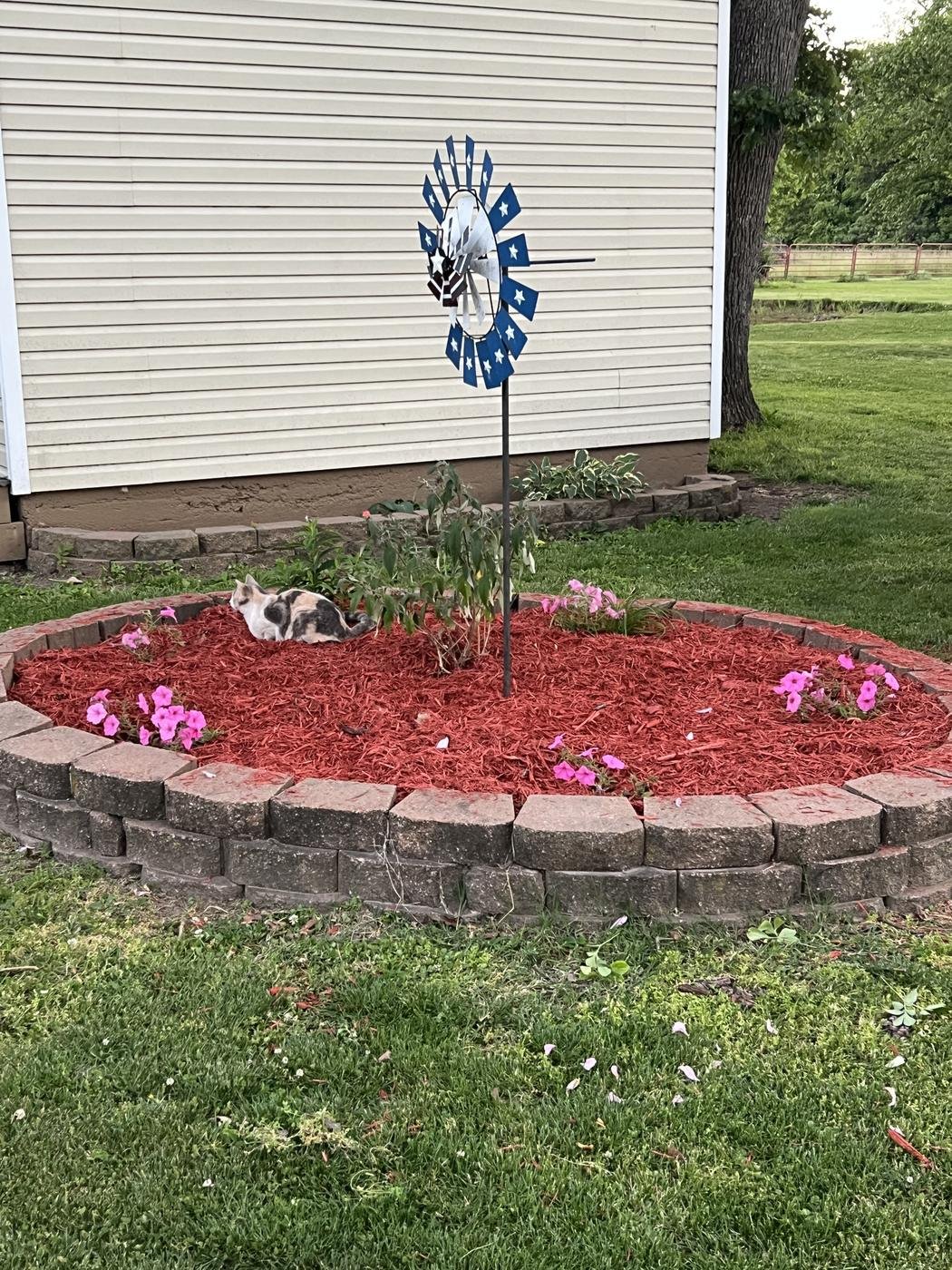 Round flower bed with stacked block edging, red mulch and pink flowers
